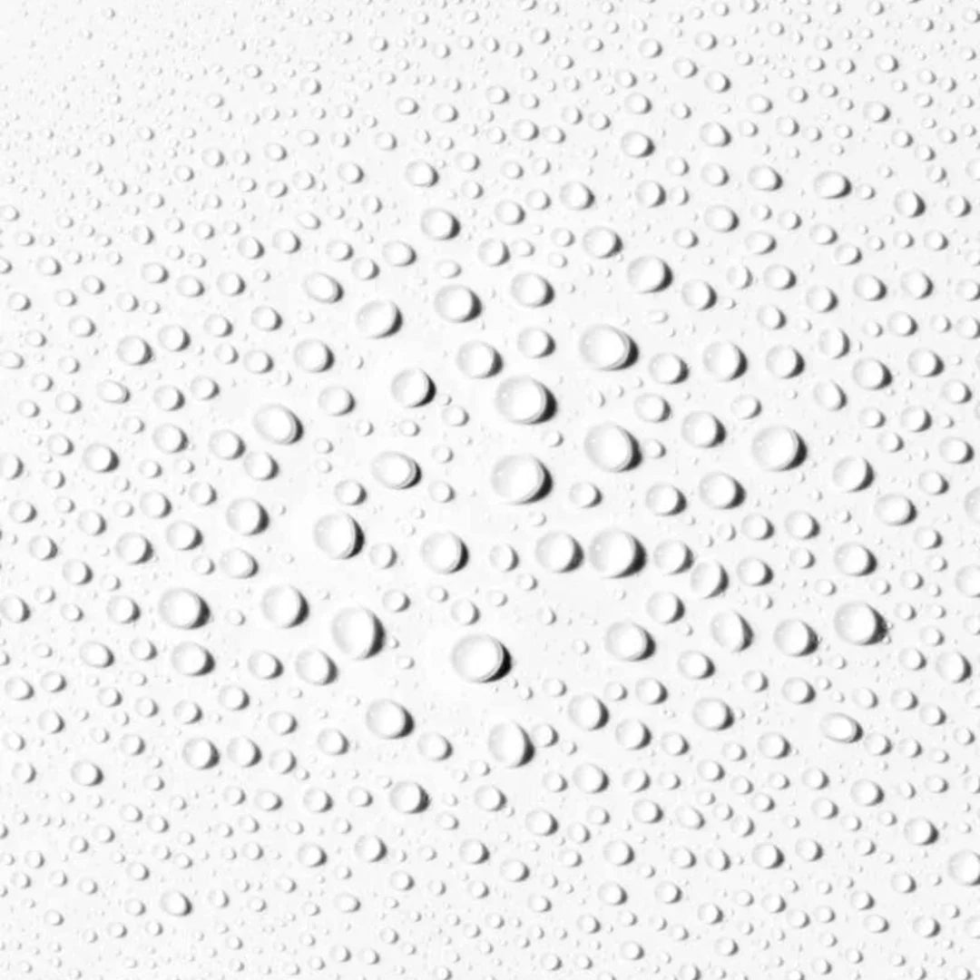 Close-up of numerous clear water droplets on a smooth white surface, showing natural reflections